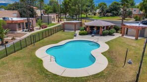 A swimming pool with a curved edge, surrounded by a fenced area with grass and trees. - Trendy Cozy Townhome with Pool (Tucson)