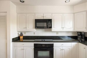 A kitchen with white cabinets, a black microwave, a stove, and a coffee maker. - Sonoran Paradise with Pool (Tucson)