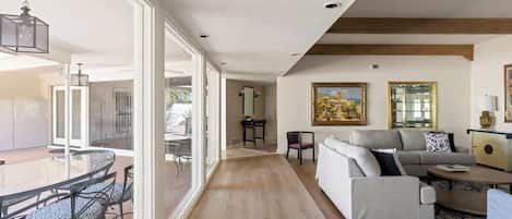 A spacious living area with a glass dining table, a sofa, and a painting on the wall.