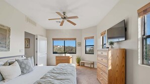 A bedroom with a bed, a ceiling fan, a dresser, a TV, and large windows. - Quiet Desert Haven- 5 mins to Starr Pass (Tucson)