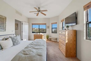 A bedroom with a bed, a ceiling fan, a dresser, a TV, and large windows. - Quiet Desert Haven- 5 mins to Starr Pass (Tucson)