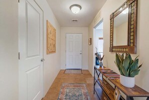 Un pasillo con una puerta blanca, un tapete, una consola de madera con una planta y un espejo.