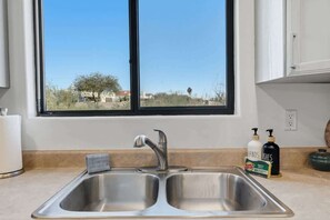 A kitchen with a double sink, a window with a view of a residential area, and two soap dispensers on the counter. - Quiet Desert Haven- 5 mins to Starr Pass (Tucson)