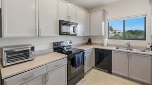 A kitchen with white cabinets, a toaster, an oven, a dishwasher, and a window with a view. - Quiet Desert Haven- 5 mins to Starr Pass (Tucson)