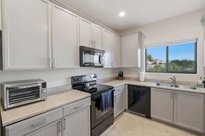 A kitchen with white cabinets, a toaster, an oven, a dishwasher, and a window with a view. - Quiet Desert Haven- 5 mins to Starr Pass (Tucson)