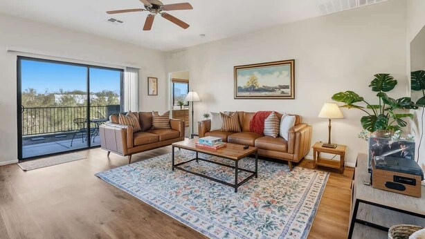 A spacious living room with a large sliding glass door to the outside, a ceiling fan, a coffee table, and a TV stand. - Quiet Desert Haven- 5 mins to Starr Pass (Tucson)