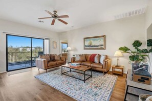 A spacious living room with a large sliding glass door to the outside, a ceiling fan, a coffee table, and a TV stand. - Quiet Desert Haven- 5 mins to Starr Pass (Tucson)