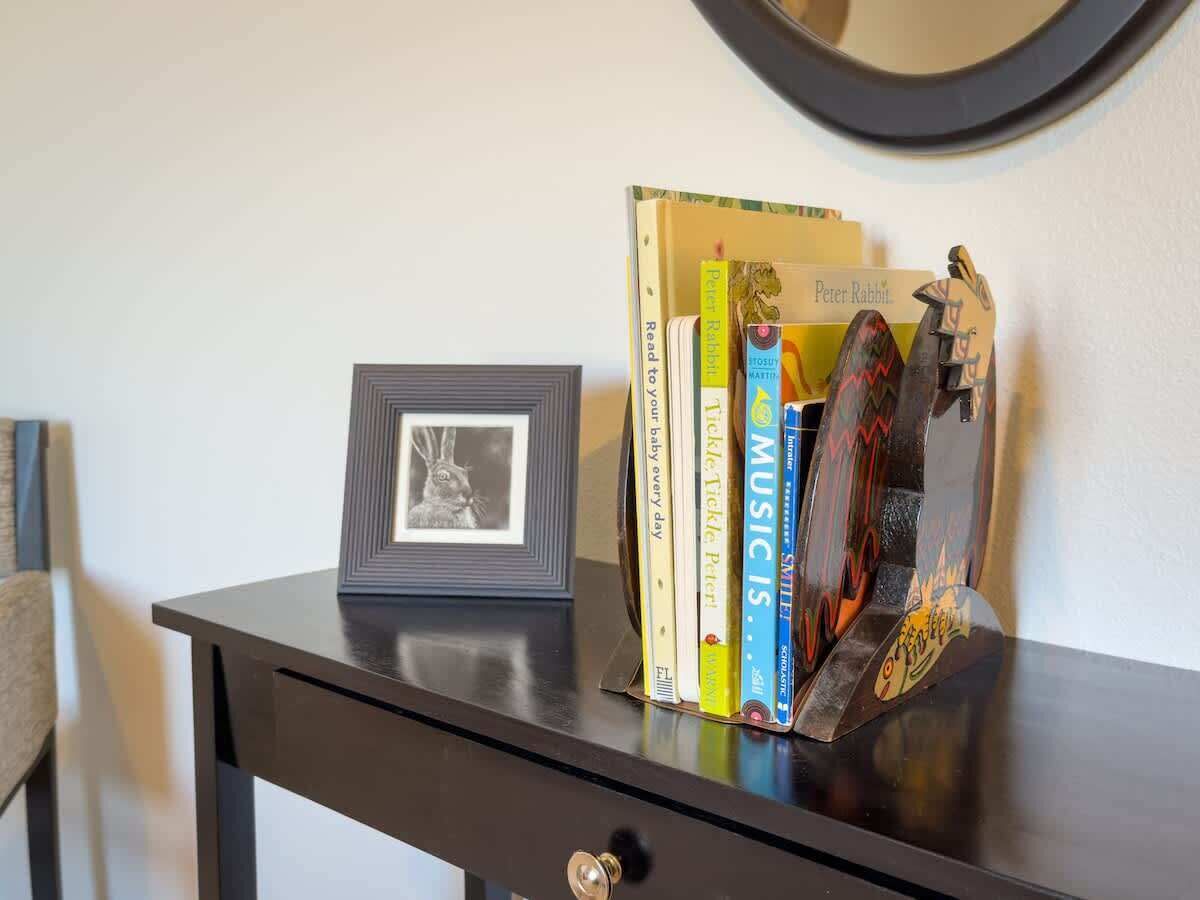 Uma mesa com um quadro emoldurado, um livro intitulado 'Leia para o seu bebê todos os dias' e um livro intitulado 'MÚSICA É' em uma estante.