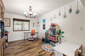 Ein Zimmer mit Holzboden, einem weißen Tisch, einem Fenster, einem Deckenventilator und einem Bücherregal.