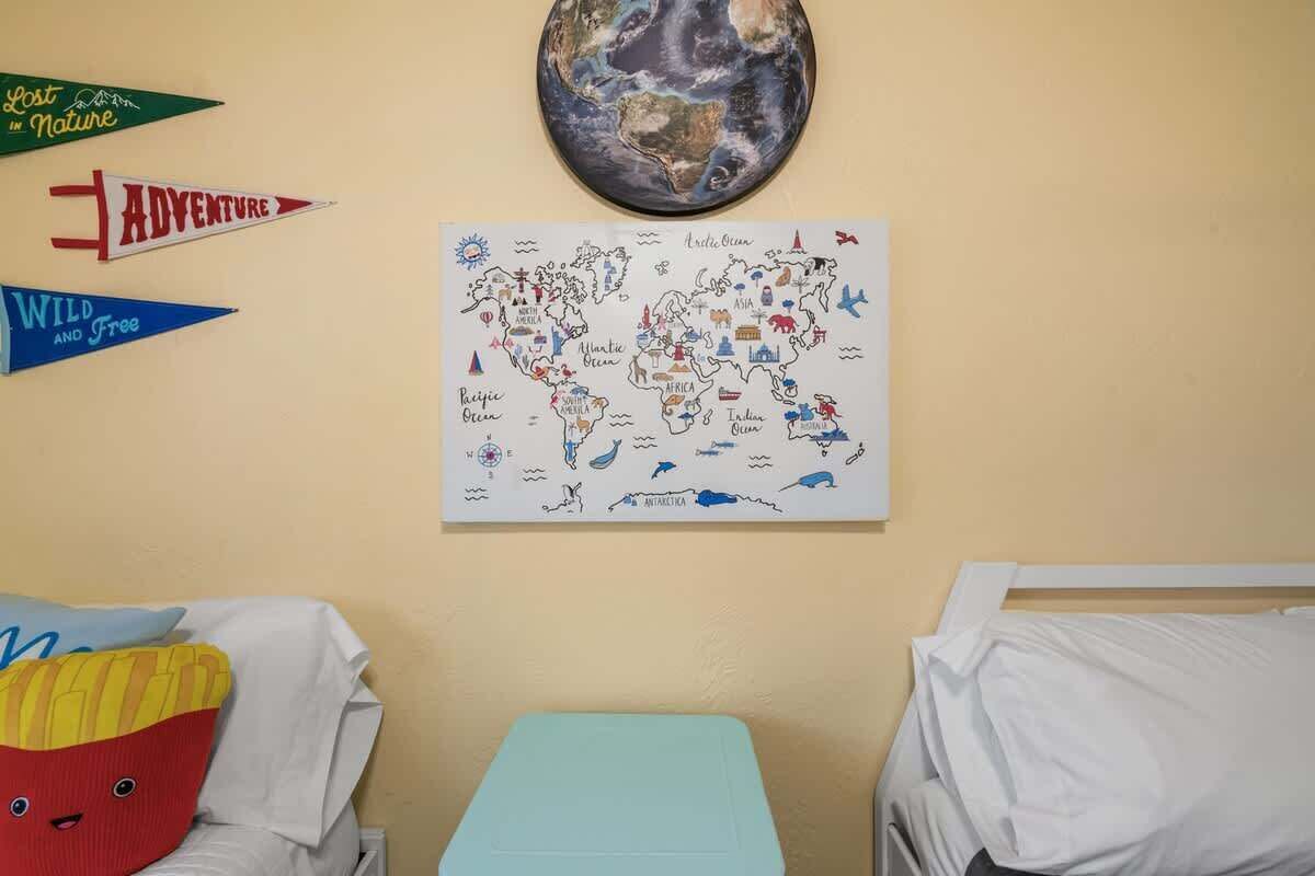 Une chambre avec deux lits, une carte du monde accrochée au mur et des guirlandes décoratives en forme de fanions.