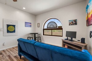 Ein Wohnzimmer mit einem blauen Sofa, einem Fernseher, einem kleinen Tisch und einem dekorativen Fenster.