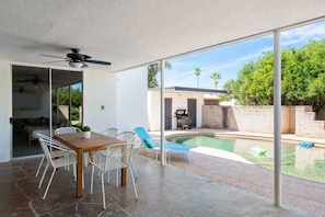 Eine Terrass mit Esstisch und Stühlen, ein Pool und Blick auf einen Hinterhof mit Grillplatz.