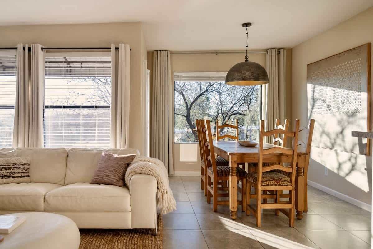 A living room with a sofa, dining table, chairs, and a large window with curtains.