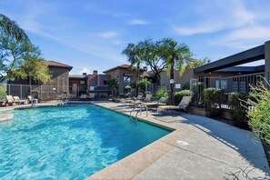 A swimming pool with lounge chairs, a fenced area, and buildings in the background. - Sanctuary Escape with Heated Pools & Views (Tucson)