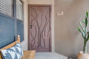 A door with a cactus design, a wooden bench with a patterned cushion, and a potted plant. - Sanctuary Escape with Heated Pools & Views (Tucson)