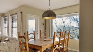 Et spiseområde med et træbord og stole, en hængende lampe samt udsigt gennem et vindue.