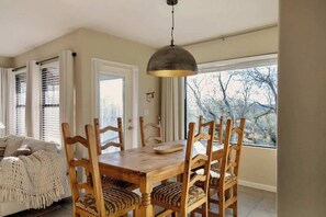 A dining area with a wooden table and chairs, a hanging light fixture, and a view through a window. - Sanctuary Escape with Heated Pools & Views (Tucson)