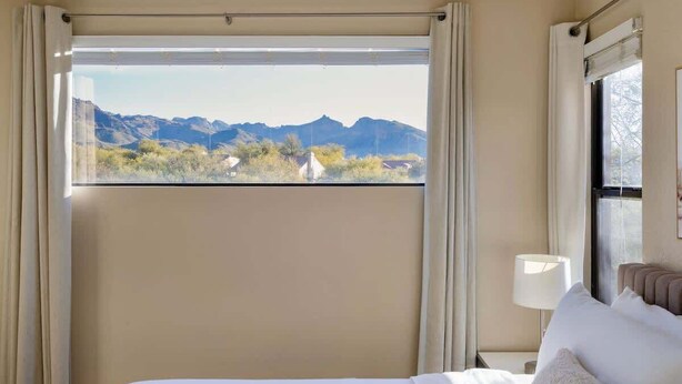 Et hotelværelse med stort vindue, seng, sengebord og lampe.