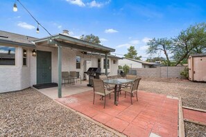 A covered patio area with a barbecue grill, outdoor seating, and a gravel driveway. - Cozy & Pet Friendly & Peloton! (Tucson)