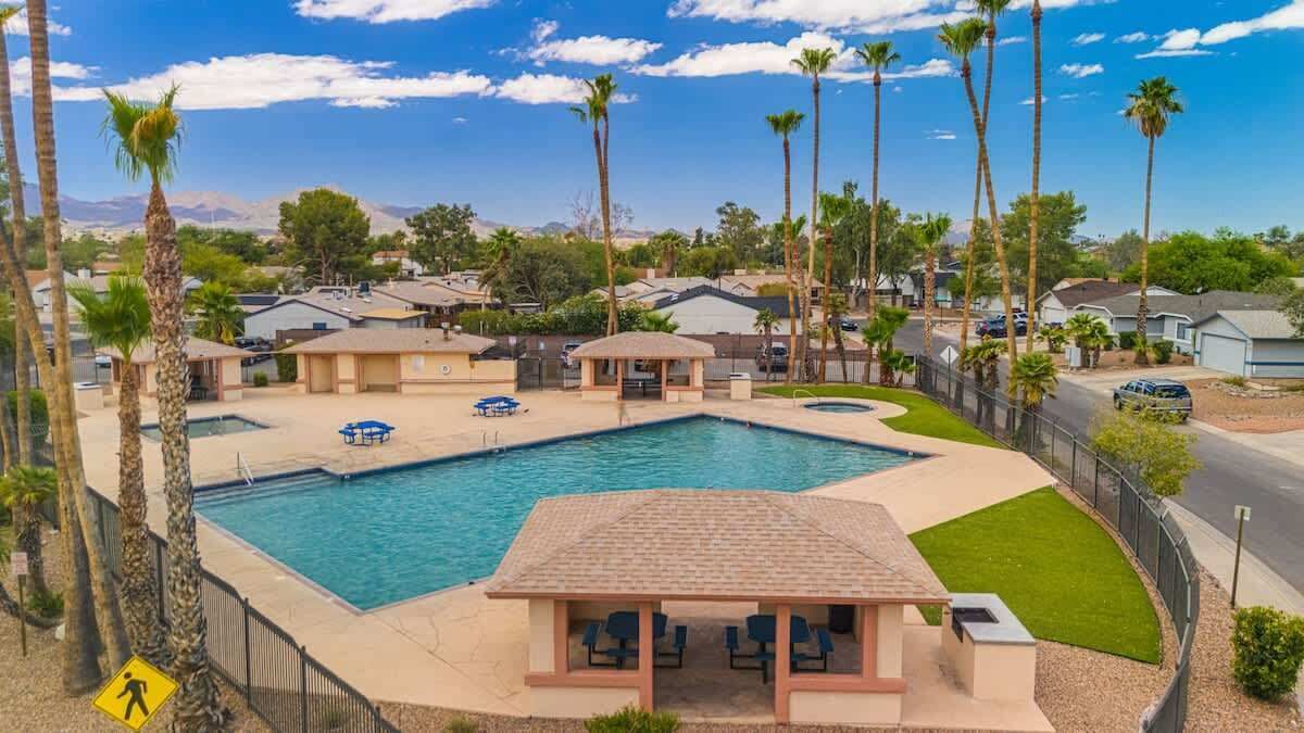 A swimming pool with lounge chairs and a gazebo, surrounded by palm trees and houses.