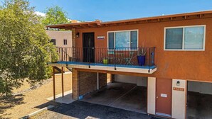 A two-story building with a balcony, a garage door, and a small garden area with potted plants. - Sunny & Bright Charm with Community Pool (Tucson)