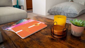 A living room with a sofa, a coffee table with a magazine, a candle, and a potted plant. - Sunny & Bright Charm with Community Pool (Tucson)