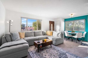 A modern living room with a sectional sofa, a coffee table, and a dining area with chairs and a table. - Sunny & Bright Charm with Community Pool (Tucson)