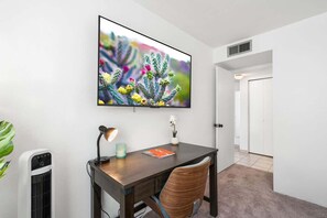 A room with a desk, a wall-mounted TV, a desk lamp, a small potted plant, and a wall-mounted heater. - Sunny & Bright Charm with Community Pool (Tucson)