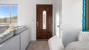 A room with a wooden door, a grey sofa, a white chair, and a window. - Sunny & Bright Charm with Community Pool (Tucson)