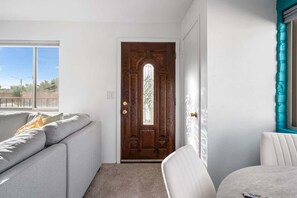 Ein Zimmer mit Holztür, einem grauen Sofa, einem weißen Sessel und einem Fenster.