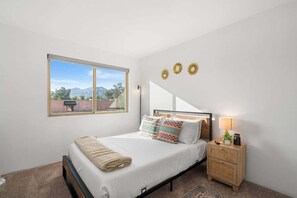 A bedroom with a bed, bedside table, lamp, and a window with a view. - Sunny & Bright Charm with Community Pool (Tucson)