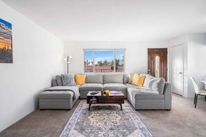 Ein modernes Wohnzimmer mit einem grauen Ecksofa, einem Couchtisch und einem gemusterten Teppich.