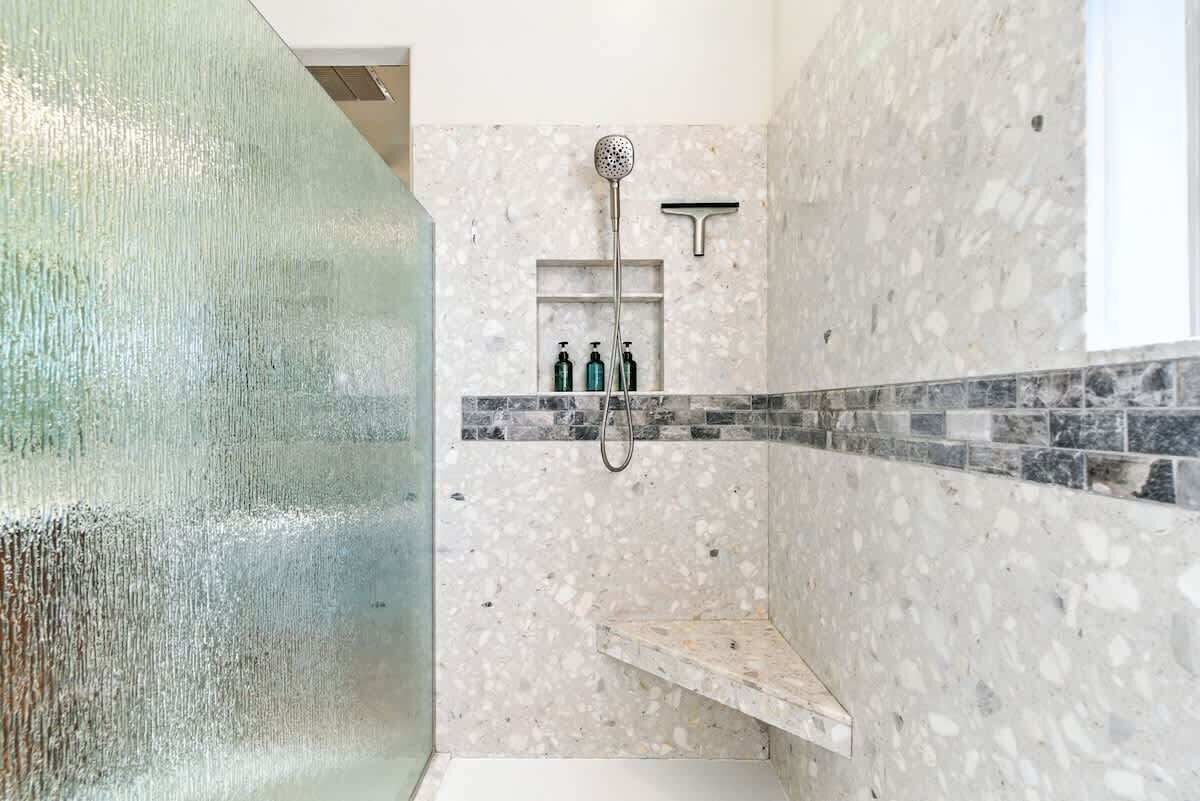 Una doccia con soffione a mano, soffione a parete e uno scaffale con articoli da toilette.