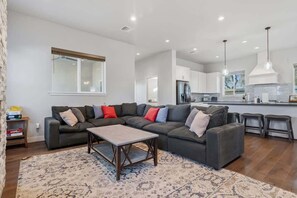 A modern living room with a sectional sofa, a coffee table, and a kitchen in the background. - Modern Tucson Home Near UA & Downtown! (Tucson)