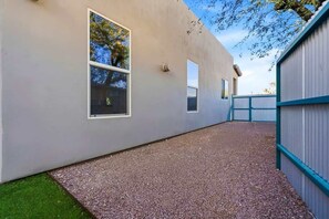 A modern building with a gravel driveway, a small grassy area, and a metal fence. - Modern Tucson Home Near UA & Downtown! (Tucson)