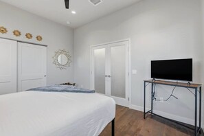 Een slaapkamer met een bed, een televisie op een standaard, een deur en een muur met decoratieve zonnespiegels.