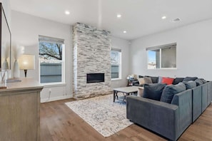 A modern living room with a stone fireplace, a grey sofa, and a dining area. - Modern Tucson Home Near UA & Downtown! (Tucson)