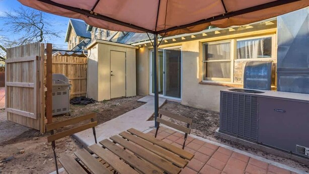 En baghave med patio, træbænk, overdækning, skur og en aircondition-enhed.