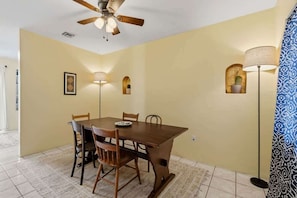 A dining area with a wooden table, chairs, a ceiling fan, wall-mounted lamps, and a patterned curtain. - Charming Barrio Adobe (Tucson)