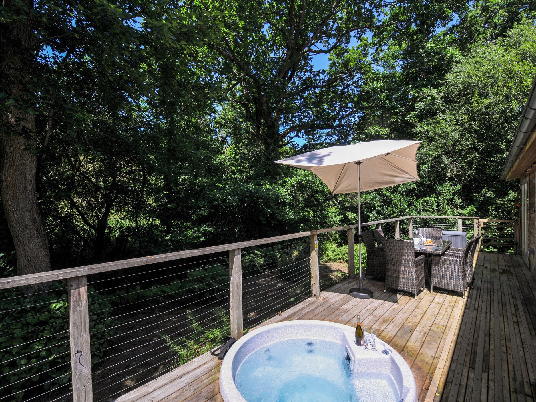 Une terrasse en bois avec un jacuzzi, du mobilier d’extérieur et une pergola surmontée d’une tonnelle.
