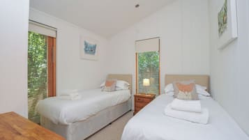 Habitación de hotel con dos camas, una mesa de madera, una mesita de noche y un ventanal con persianas.