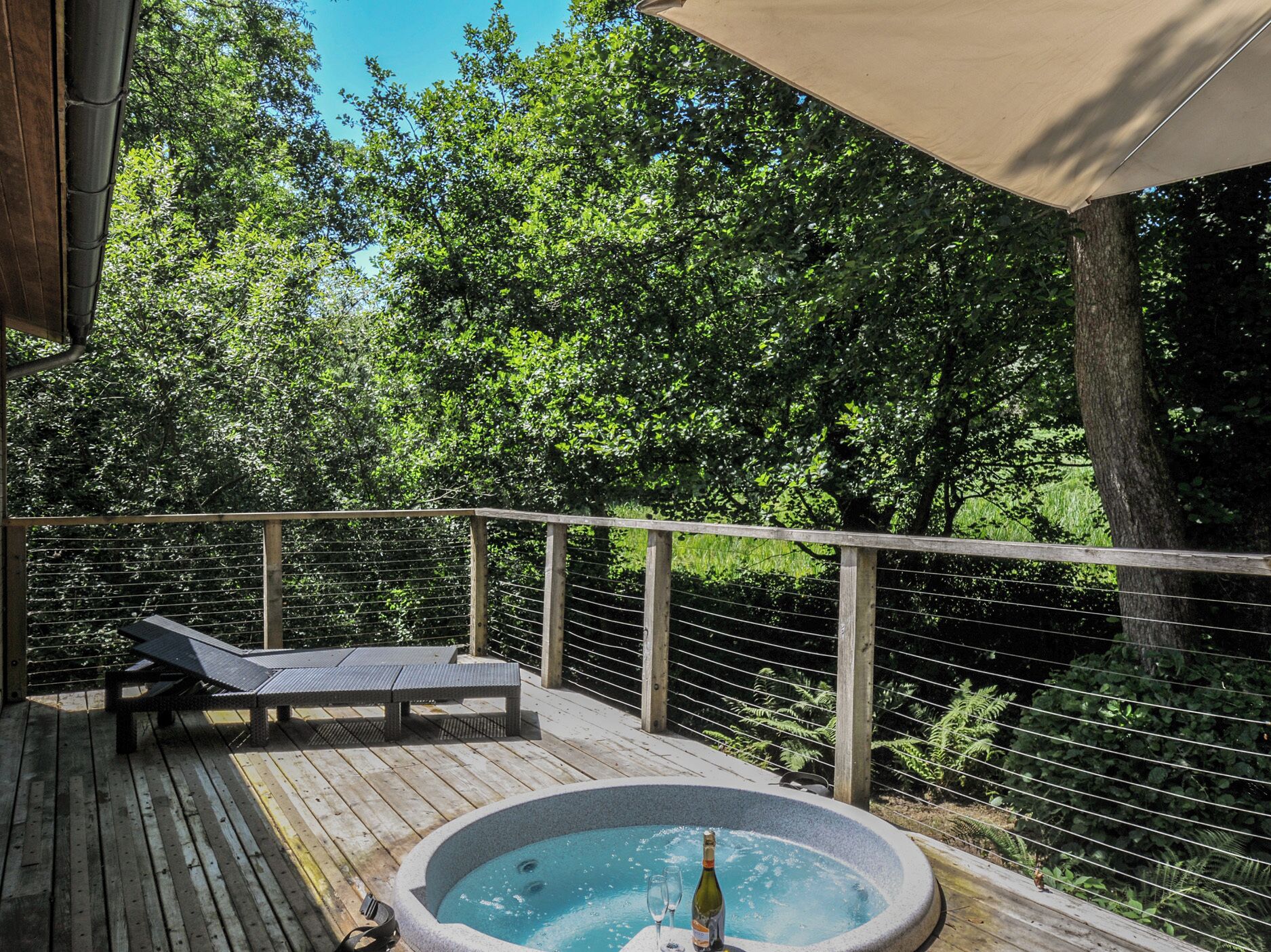 A wooden deck with a hot tub, lounge chairs, and a canopy.