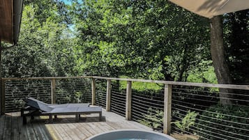 A wooden deck with a hot tub, lounge chairs, and a canopy.