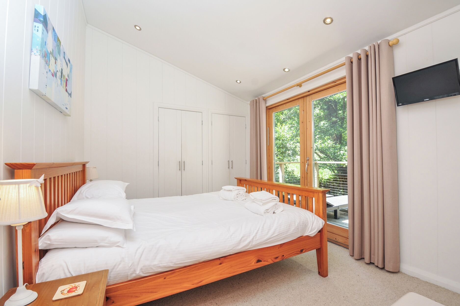 A bedroom with a wooden bed, a desk with a lamp, a TV, and a window with curtains.