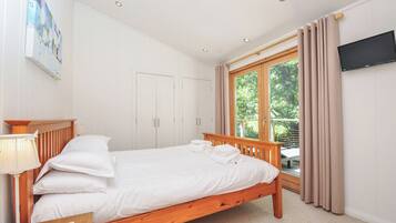 A bedroom with a wooden bed, a desk with a lamp, a TV, and a window with curtains.
