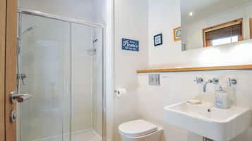 Uma casa de banho com cabine de duche em vidro, sanita, lavatório com espelho em cima e um aviso na parede.