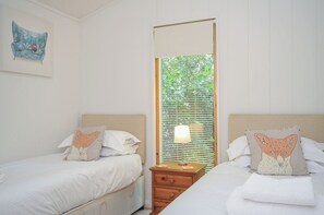 Una habitación de hotel con dos camas, una mesita de noche, una lámpara y una ventana con persianas.