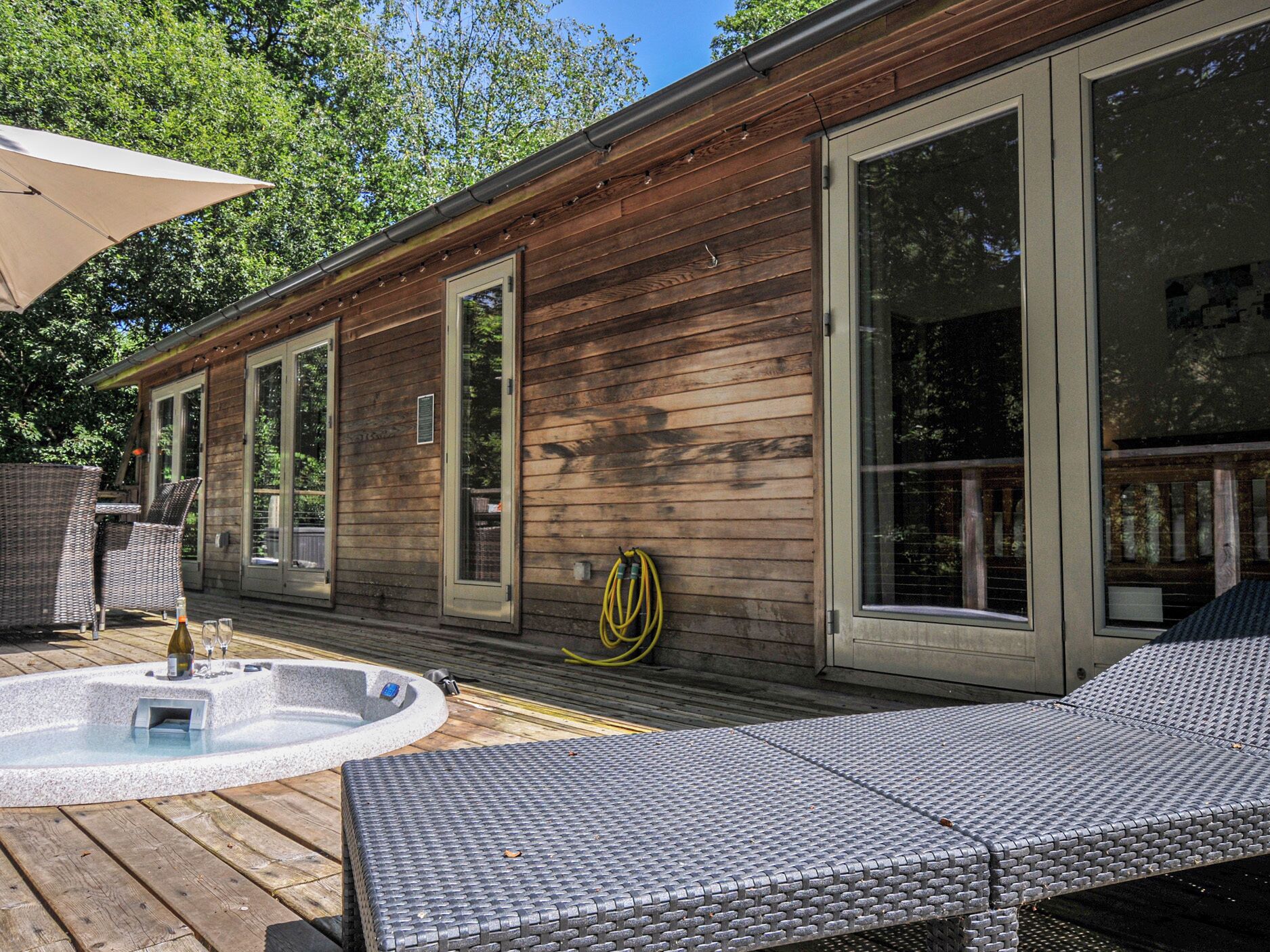 Una cabaña de madera con jacuzzi, zona de estar exterior y ventanas amplias.
