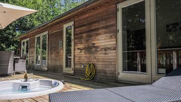 Una cabaña de madera con jacuzzi, zona de estar exterior y ventanas amplias.