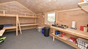Una habitación con literas, un banco de trabajo, una ventana y estantes con diversos objetos.